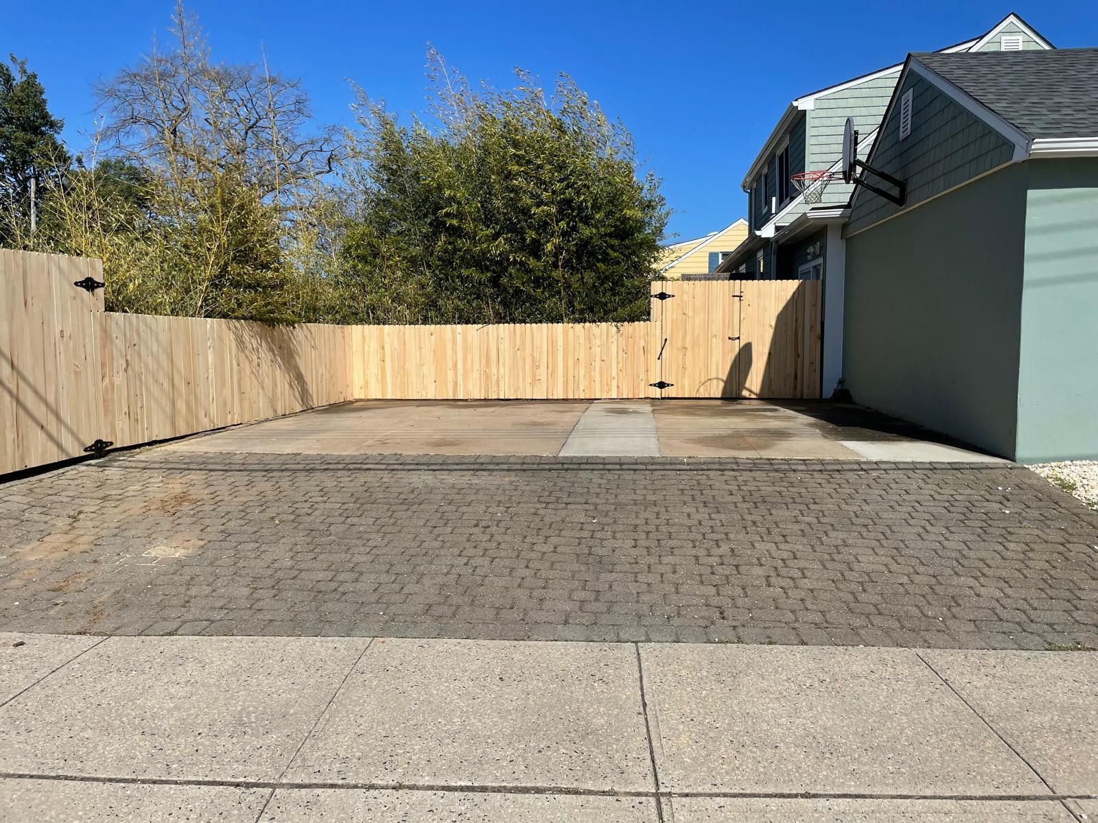A driveway with a wooden fence and a house in the background