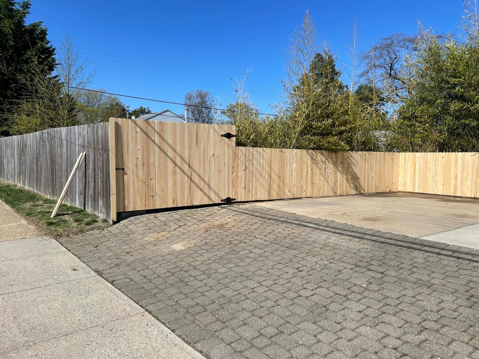 A wooden fence with a gate in the middle of a driveway.