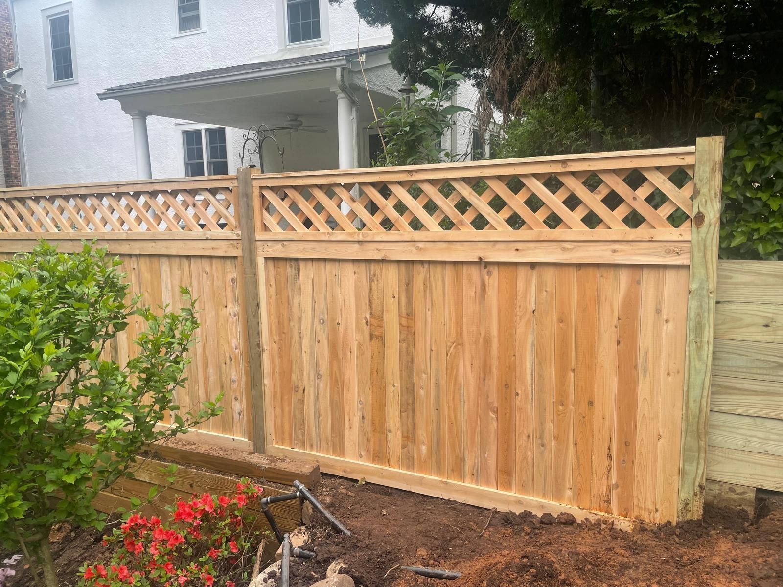 A wooden fence with a lattice design is in front of a white house.
