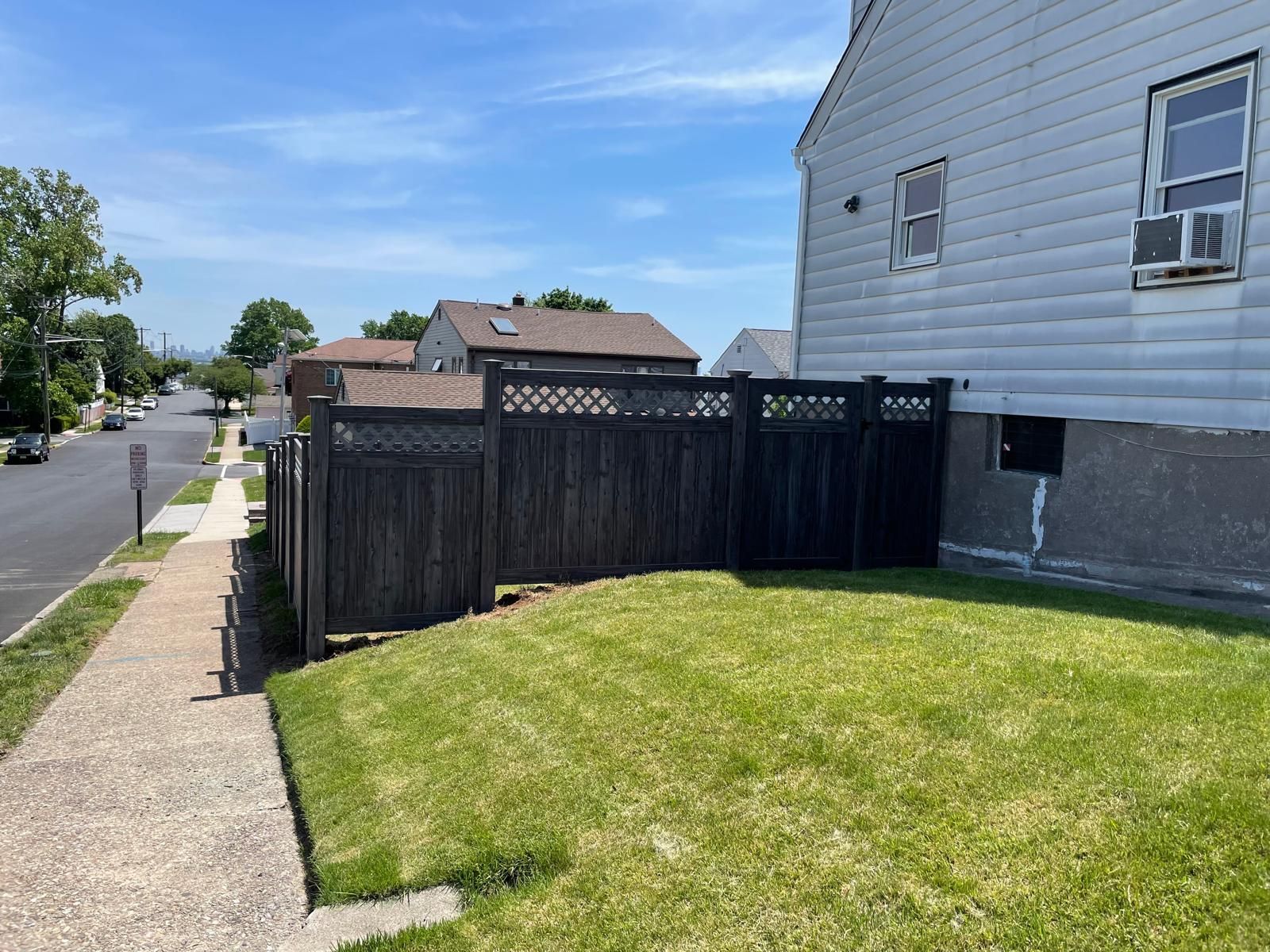 A wooden fence surrounds a lush green yard in front of a house.
