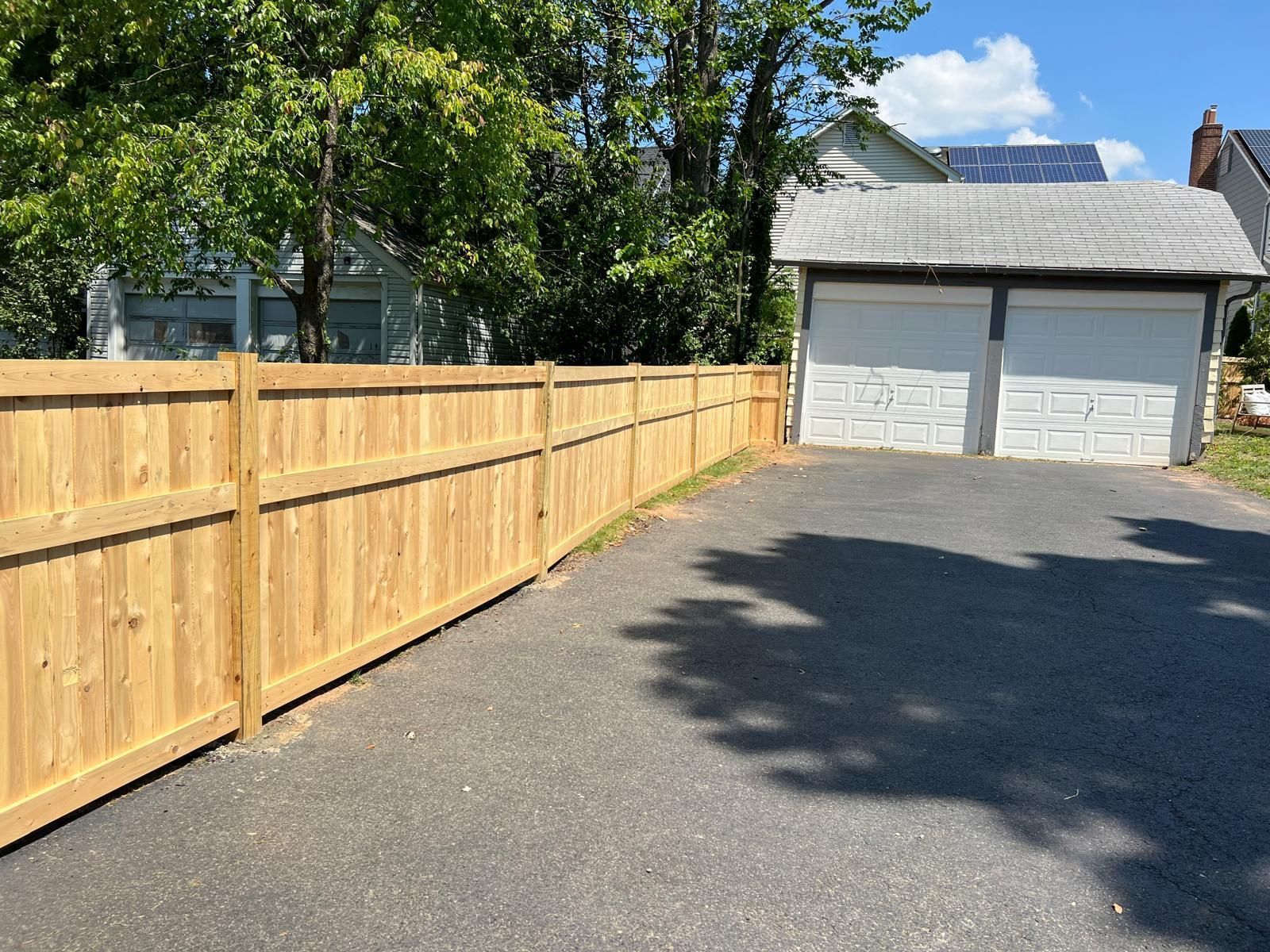 A wooden fence surrounds a driveway leading to a garage.