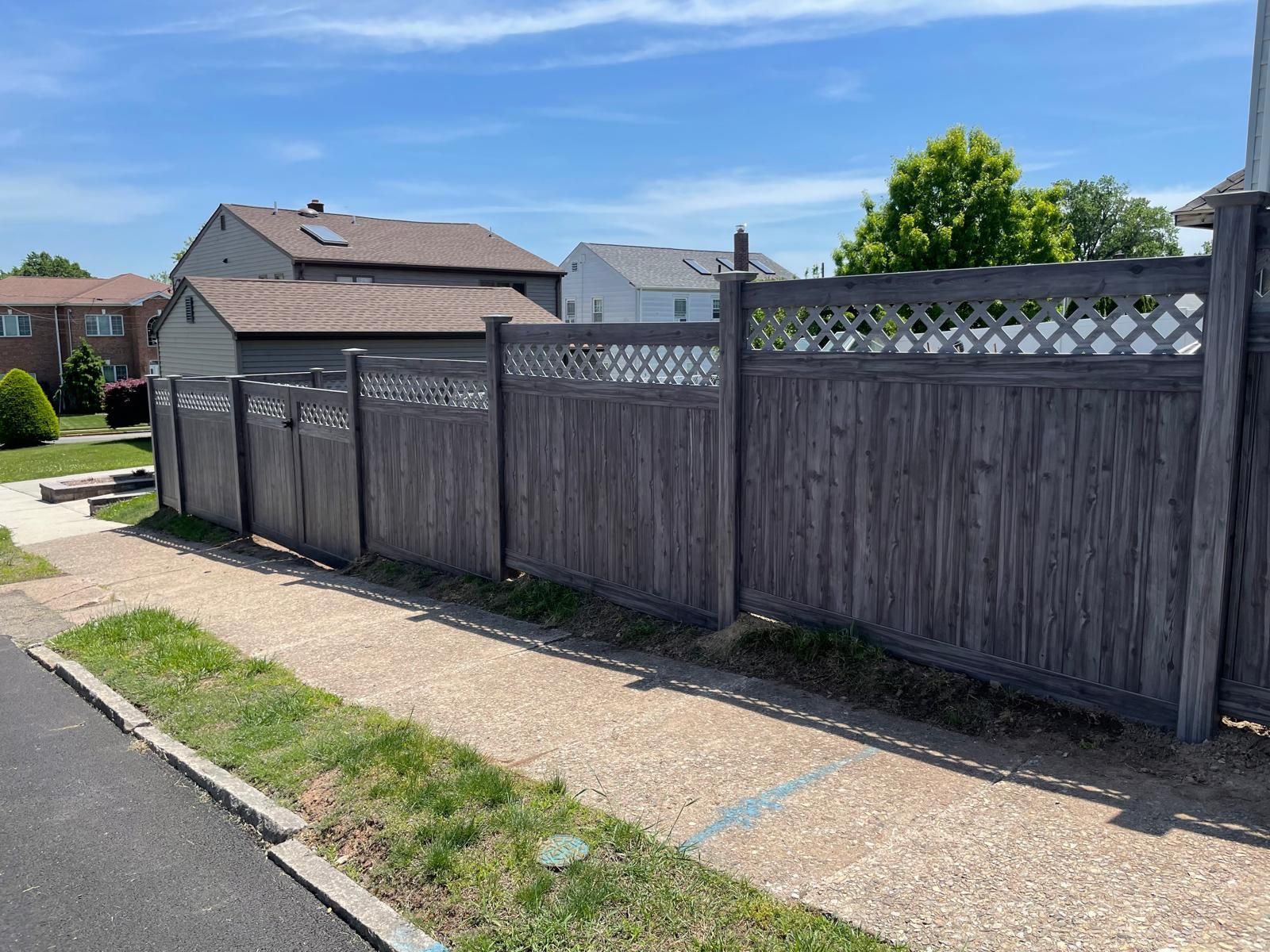 A wooden fence is sitting on the side of a road next to a sidewalk.