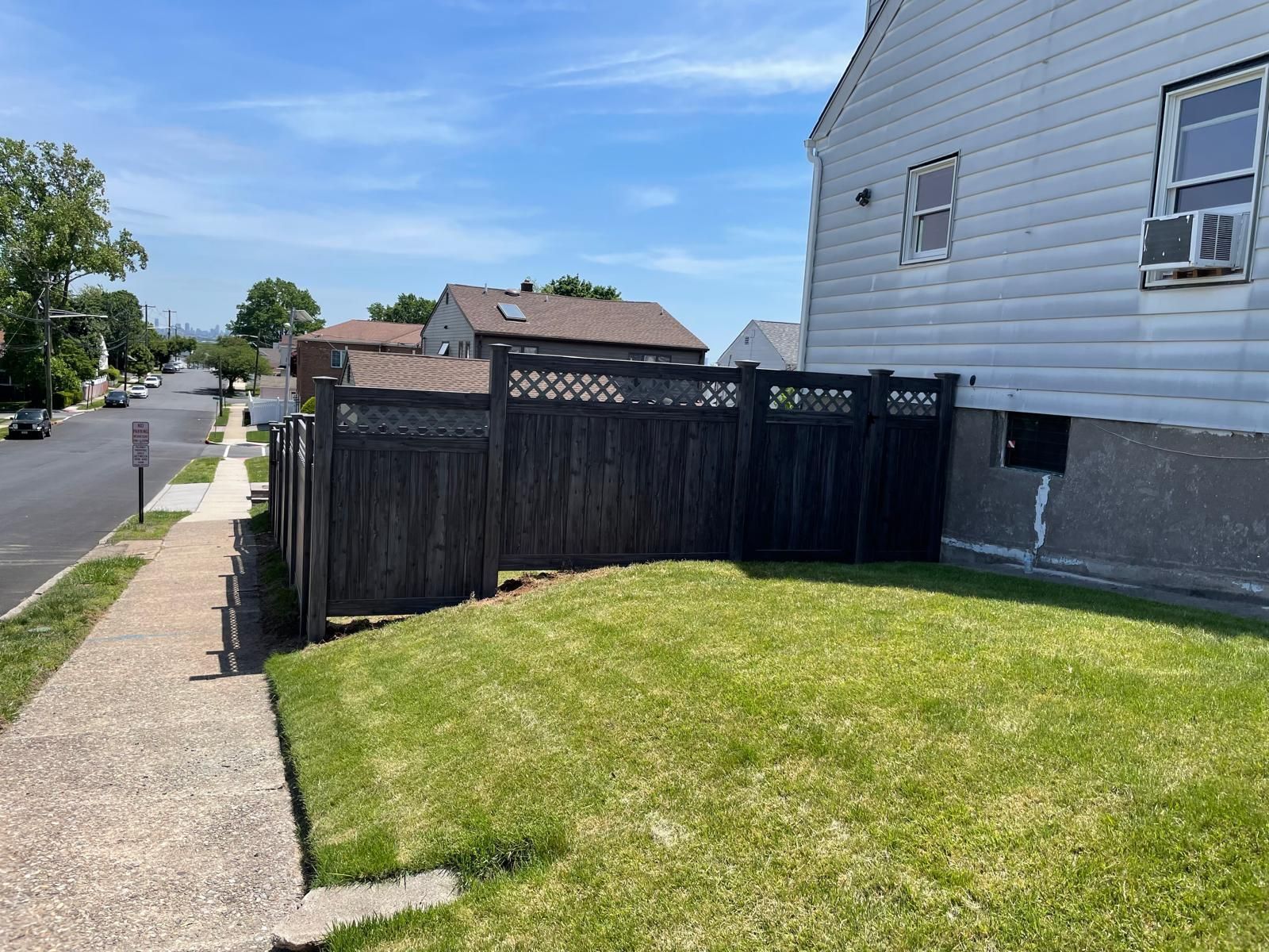 A black fence surrounds a lush green yard in front of a white house.