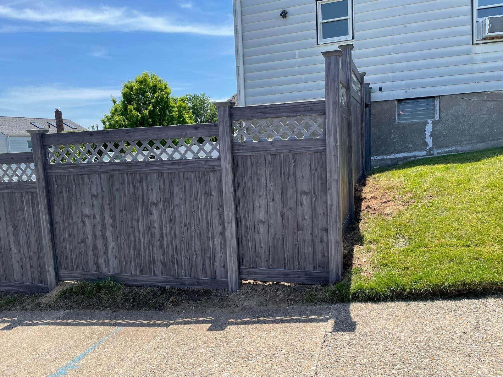 A wooden fence is sitting on the side of a road next to a house.