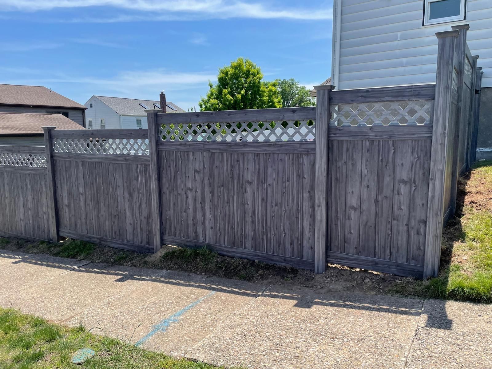 A wooden fence is sitting next to a sidewalk in front of a house.