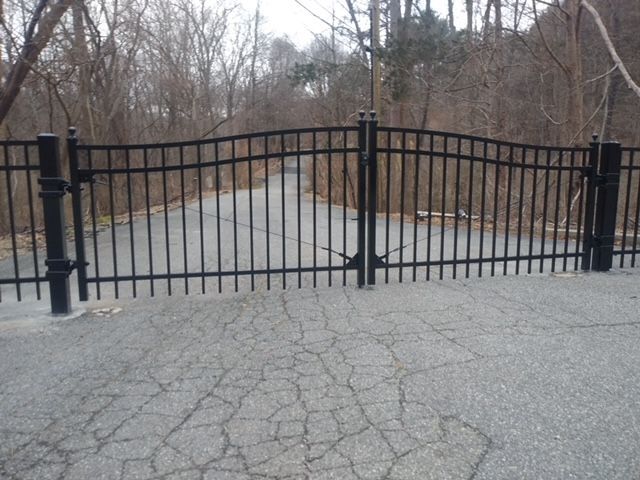 A black fence surrounds a road with trees in the background