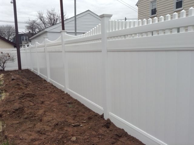 A white vinyl fence is sitting on top of a dirt hill next to a house.