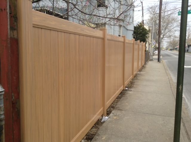 A wooden fence along a sidewalk next to a street.