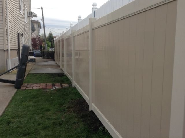 A white fence surrounds a lush green yard next to a house.