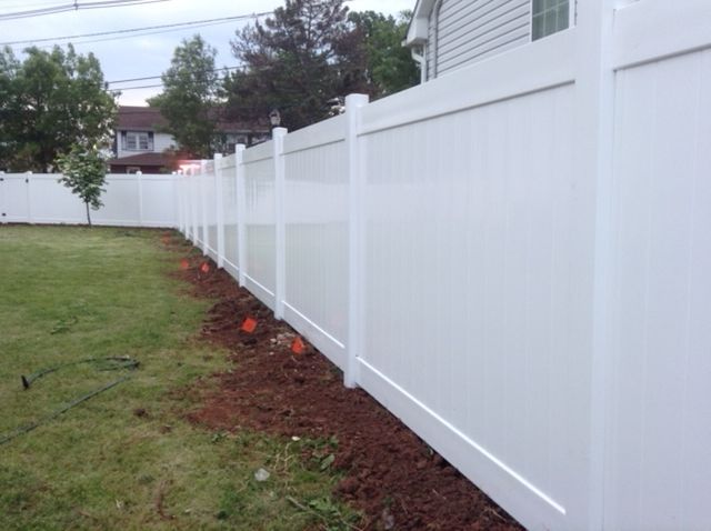 A white fence surrounds a lush green yard in front of a house.