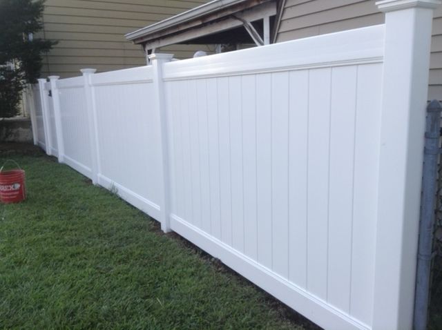 A white vinyl fence is sitting in the grass next to a house.