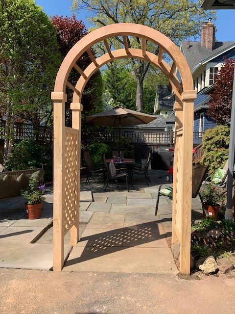 A wooden archway leading to a patio with chairs and umbrellas