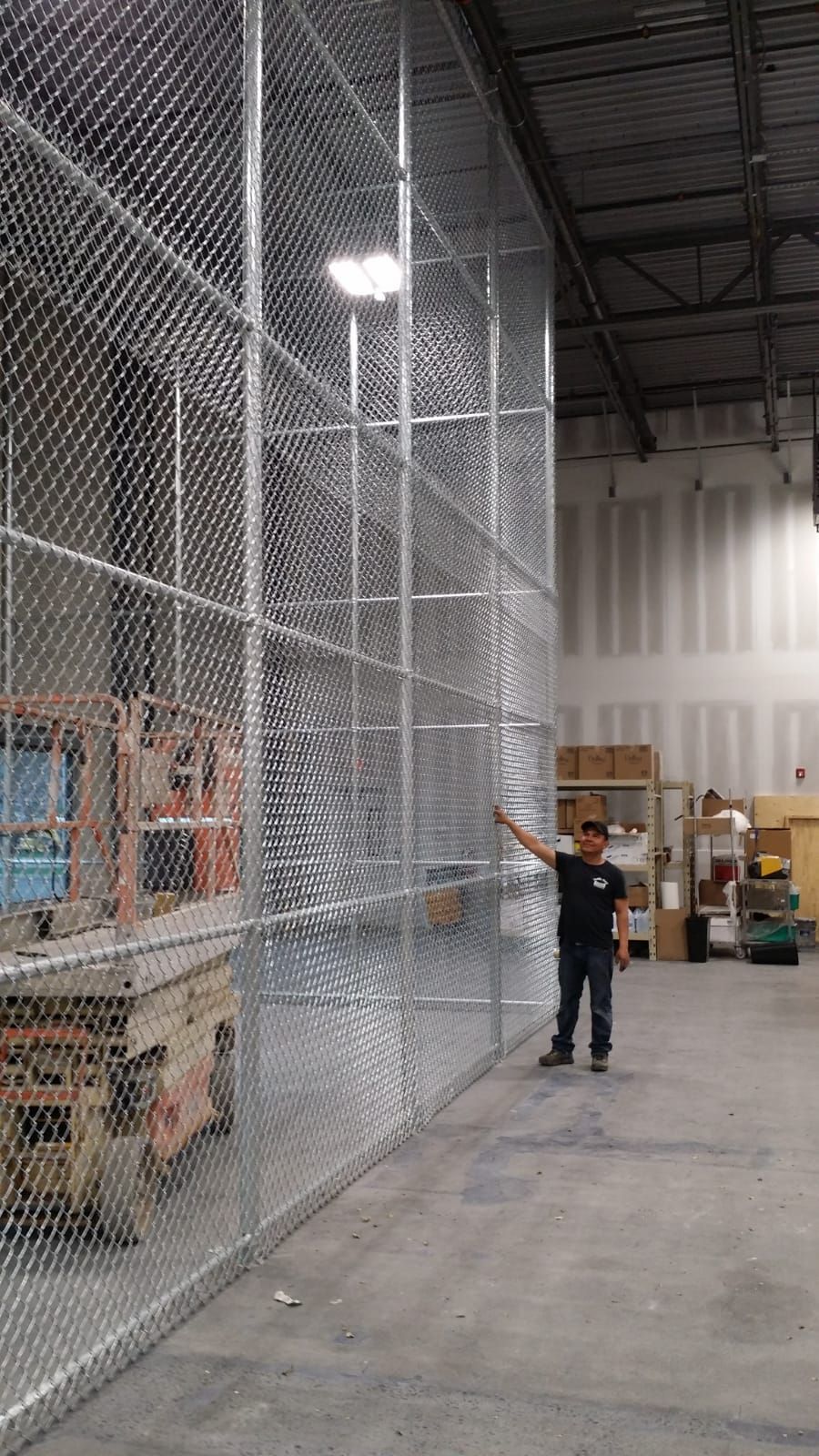A man is standing in front of a chain link fence in a warehouse.