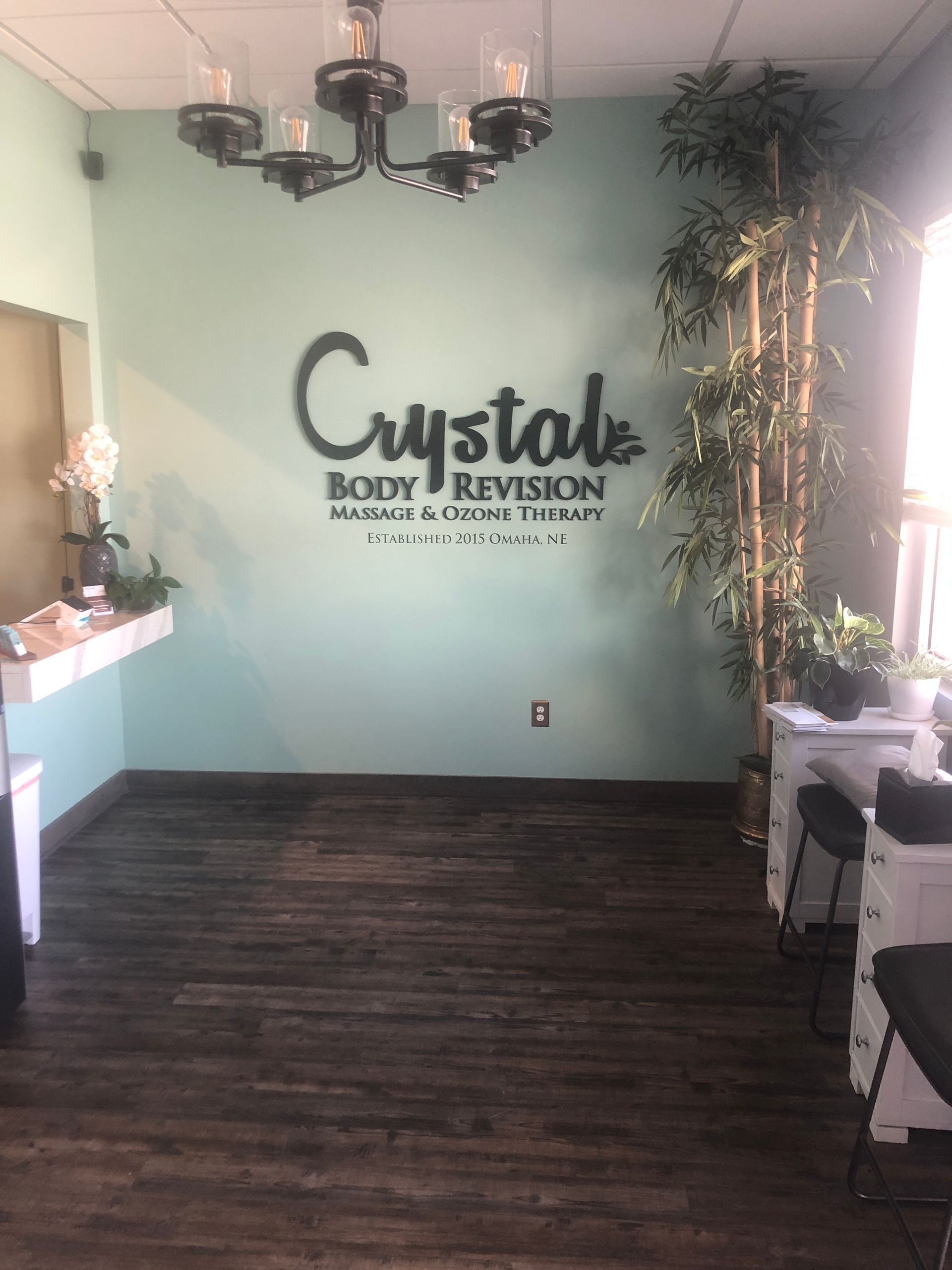 Lobby of a spa with teal walls, chandelier, wood floor, and “Crystals Body & Revision” sign.