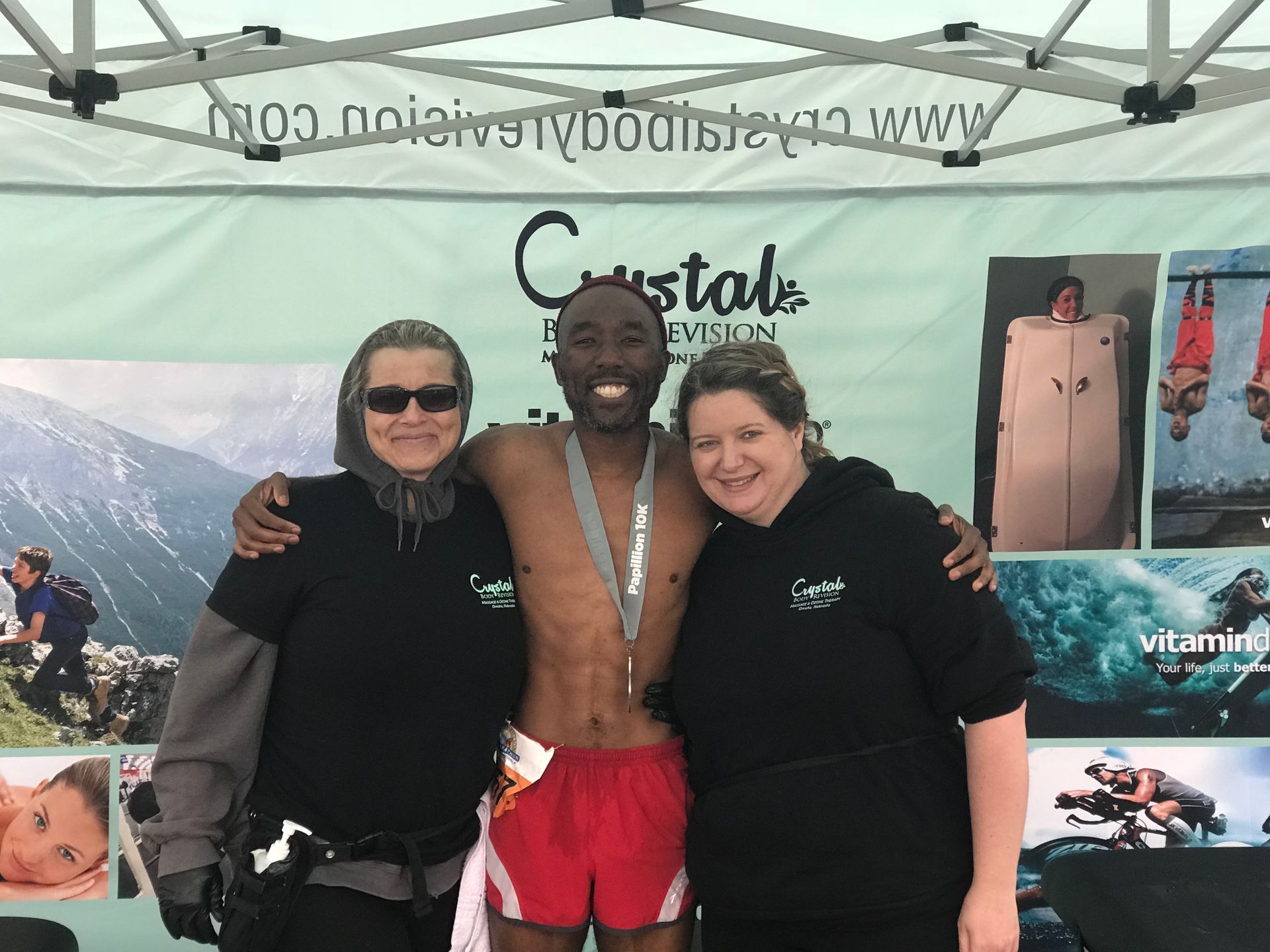 Three people posing under a Cristal canopy, with snorkeling and beach posters in the background.