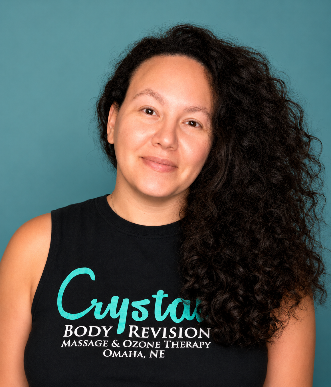 Portrait of a smiling person in a black Crystal Body Revision shirt against a teal background