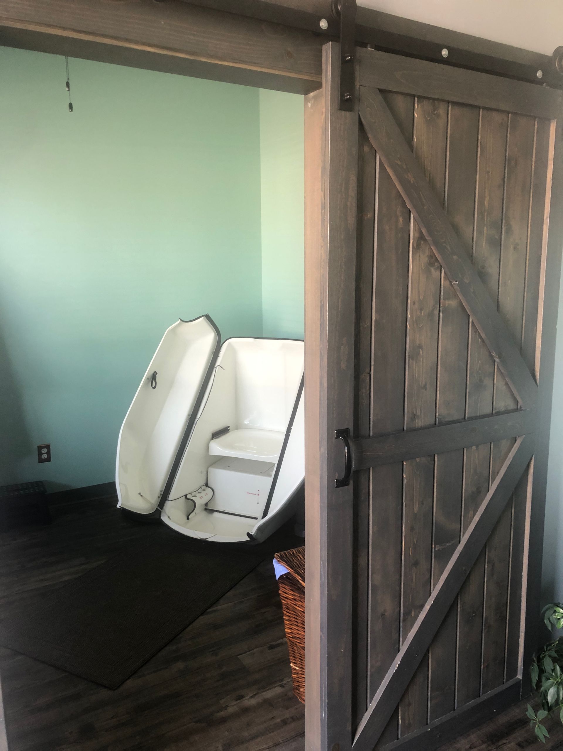 White coffin-like box in a wooden barn doorway beside a mint-green room.