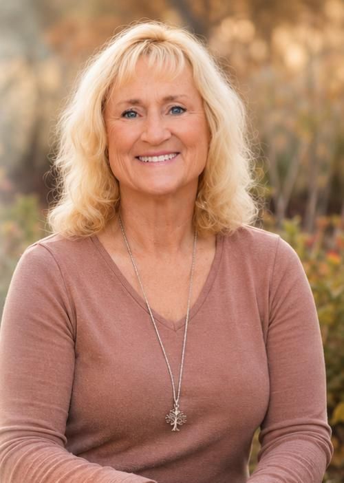 Smiling woman in a brown top standing outdoors with blurred trees in the background
