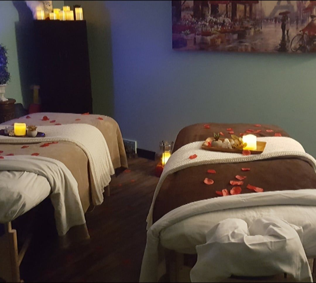 Dimly lit spa room with three massage tables, towels, candles, and rose petals.