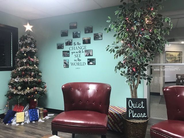 Lobby with a red chair, Christmas tree, potted tree, and a “Quiet Please” sign on teal walls.