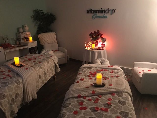 Spa room with two massage tables, lit candles, and red flower decor on white towels