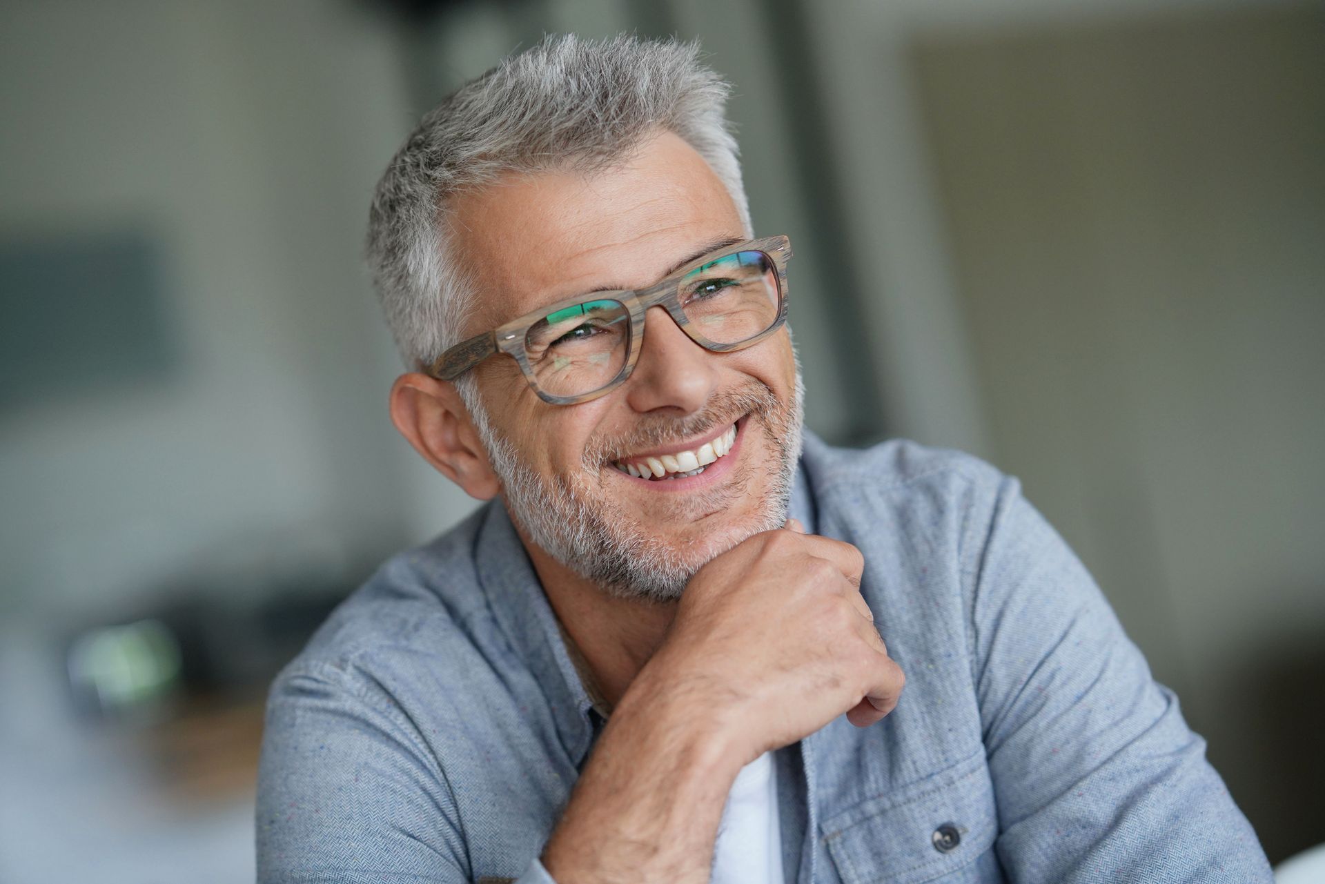 Man with gray hair and beard wearing glasses, smiling and looking up.