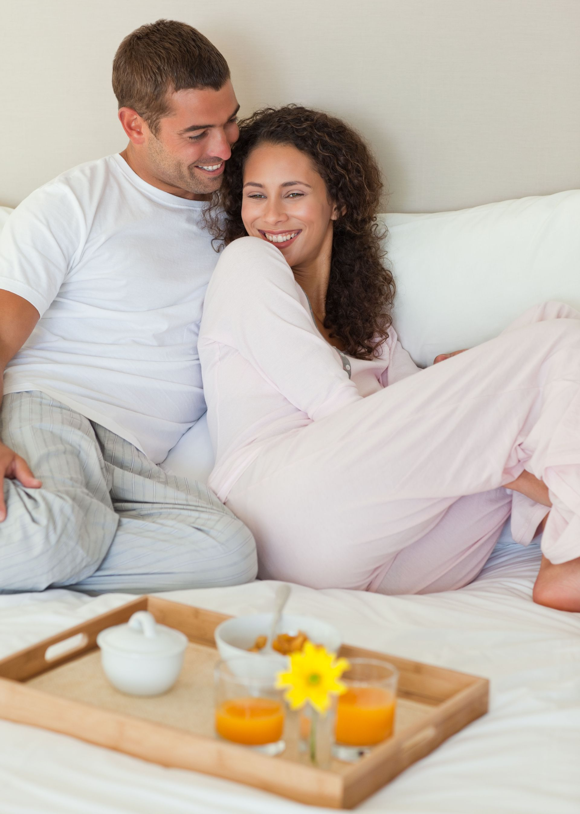Couple in pajamas smiling in bed, breakfast tray in front.