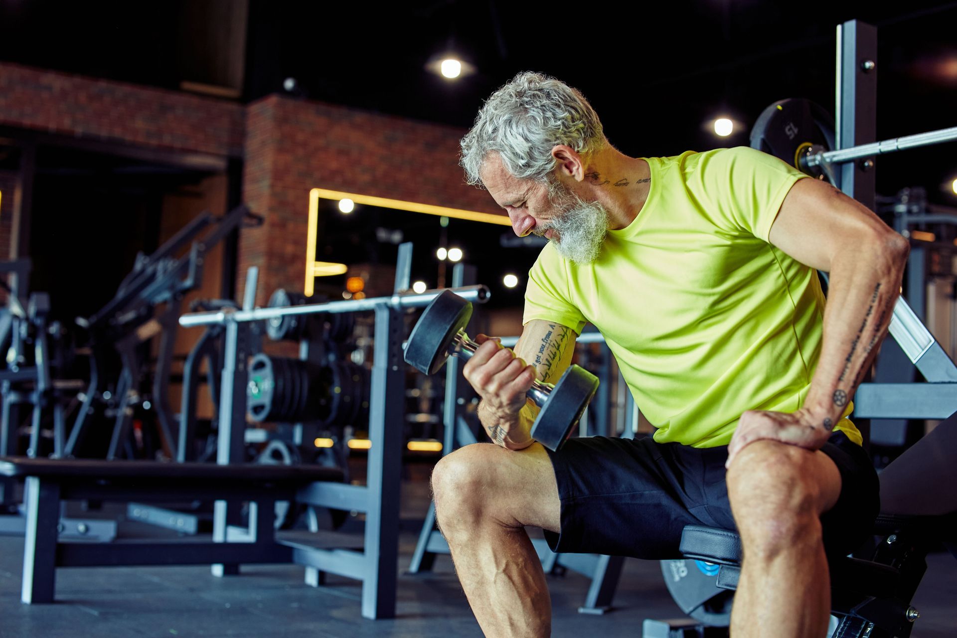 Older man with gray hair and beard lifting dumbbell at the gym.