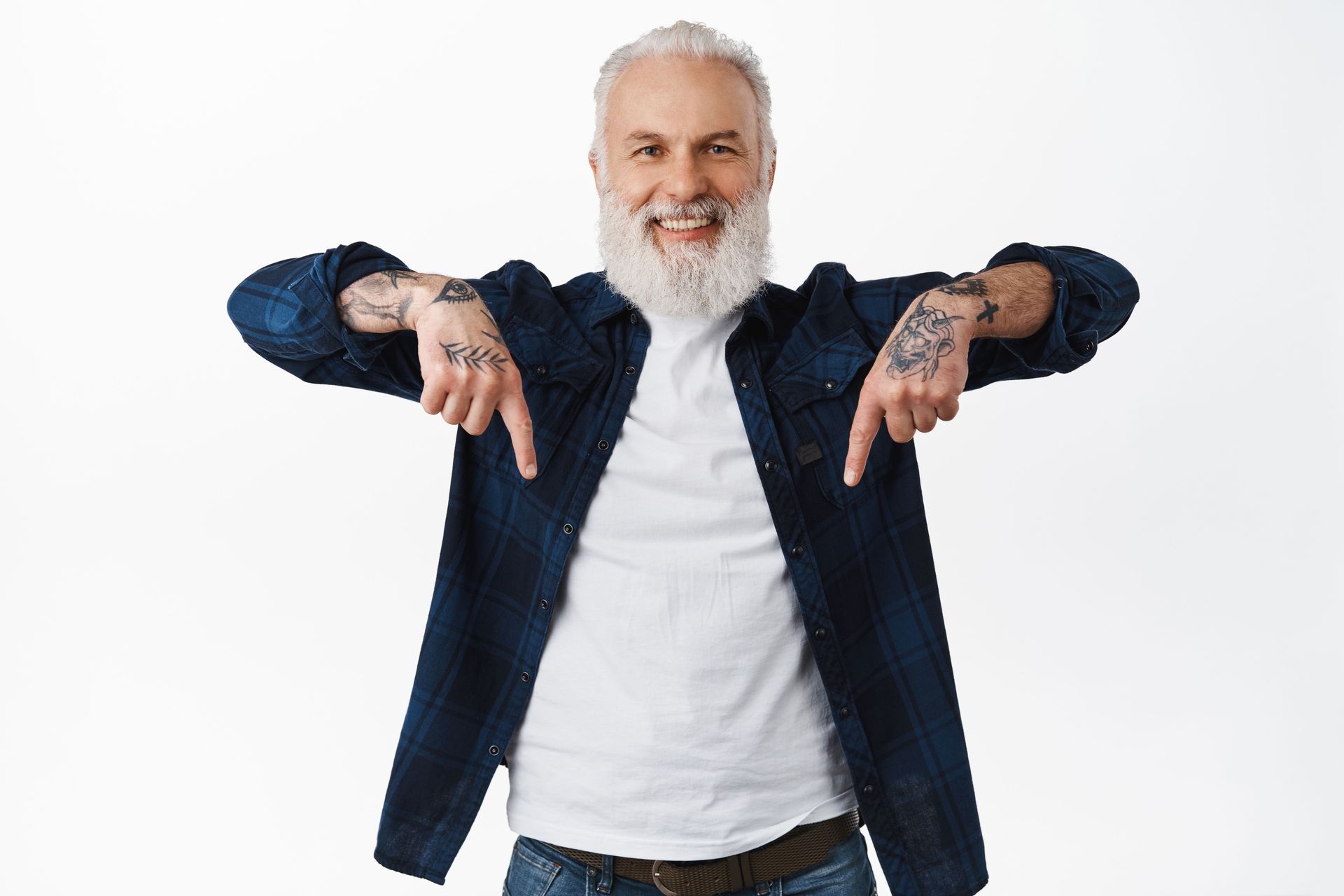 Smiling, tattooed man with a long white beard points down with both hands.