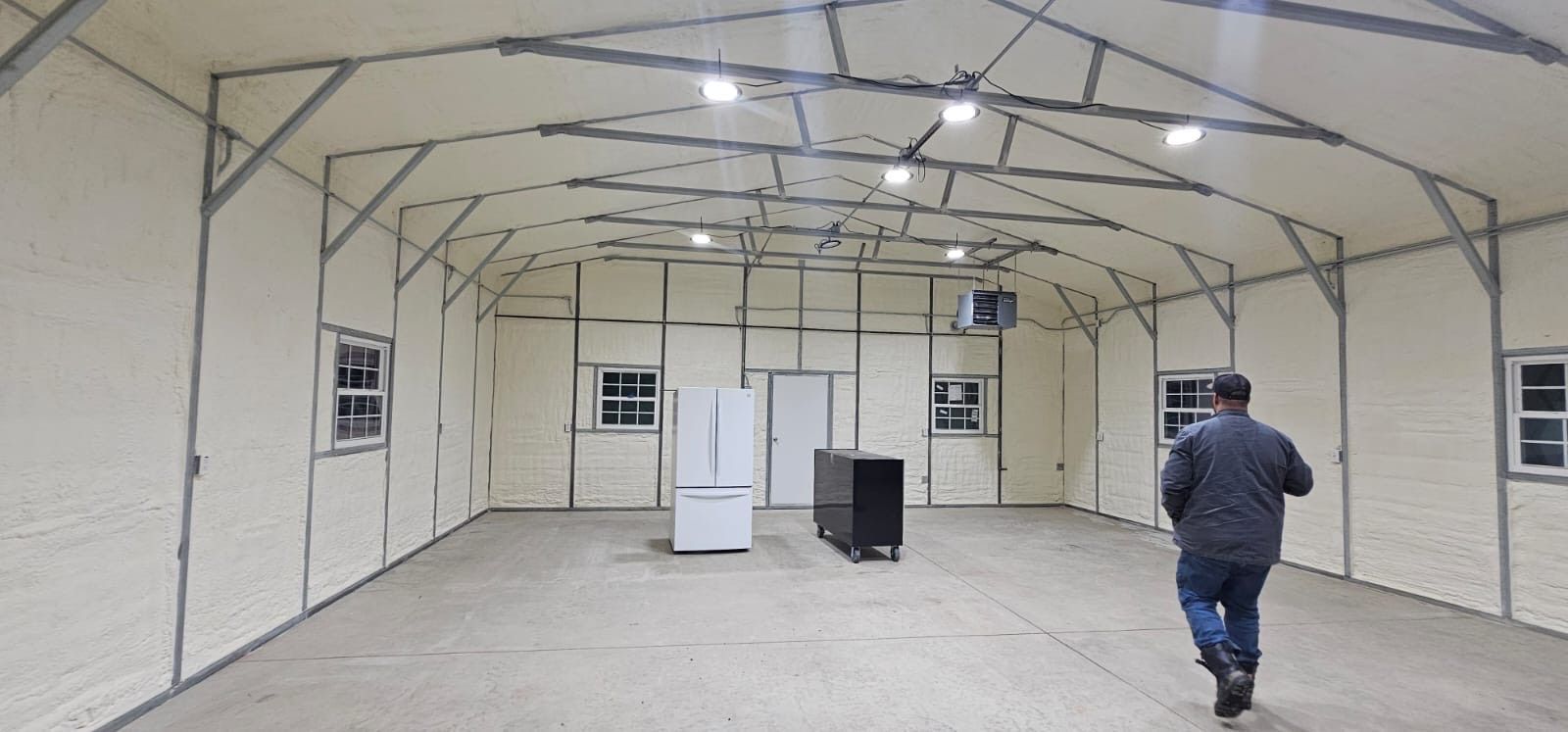 A man is walking through an empty room with a refrigerator.