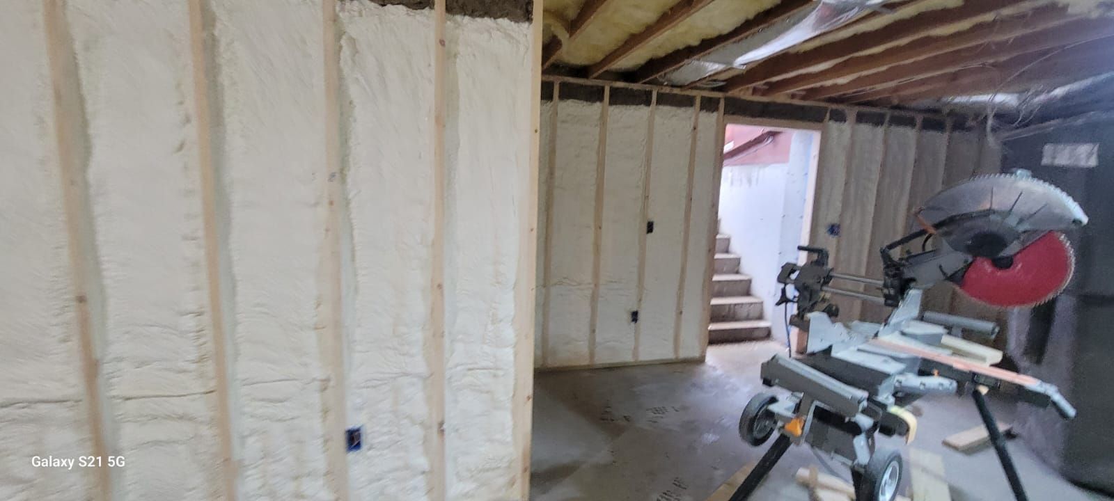 A sliding miter saw is sitting in a basement next to a wall.