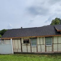 A small house with a roof and a fence is sitting in the middle of a lush green field.