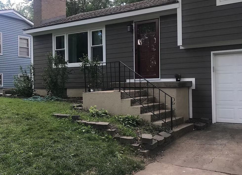 Front of a gray house with a small porch, steps, railing, garage, and grassy yard
