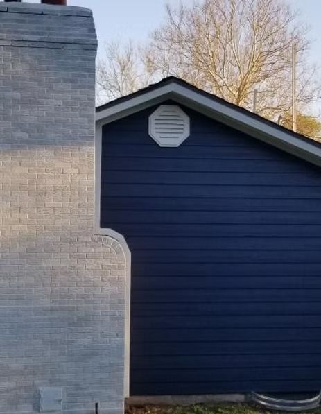 Dark blue house side wall beside a light gray chimney, with a white octagonal vent near the roofline.