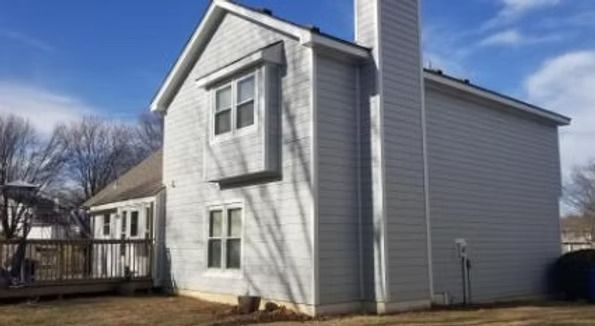 White two-story house with gray siding and windows, shown from the side under a blue sky.