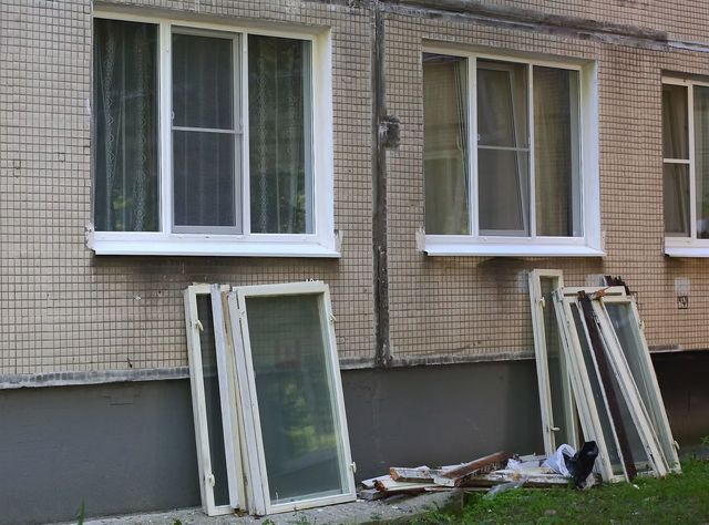 Apartment windows with white frames; several window panes lean against a brick wall below them.