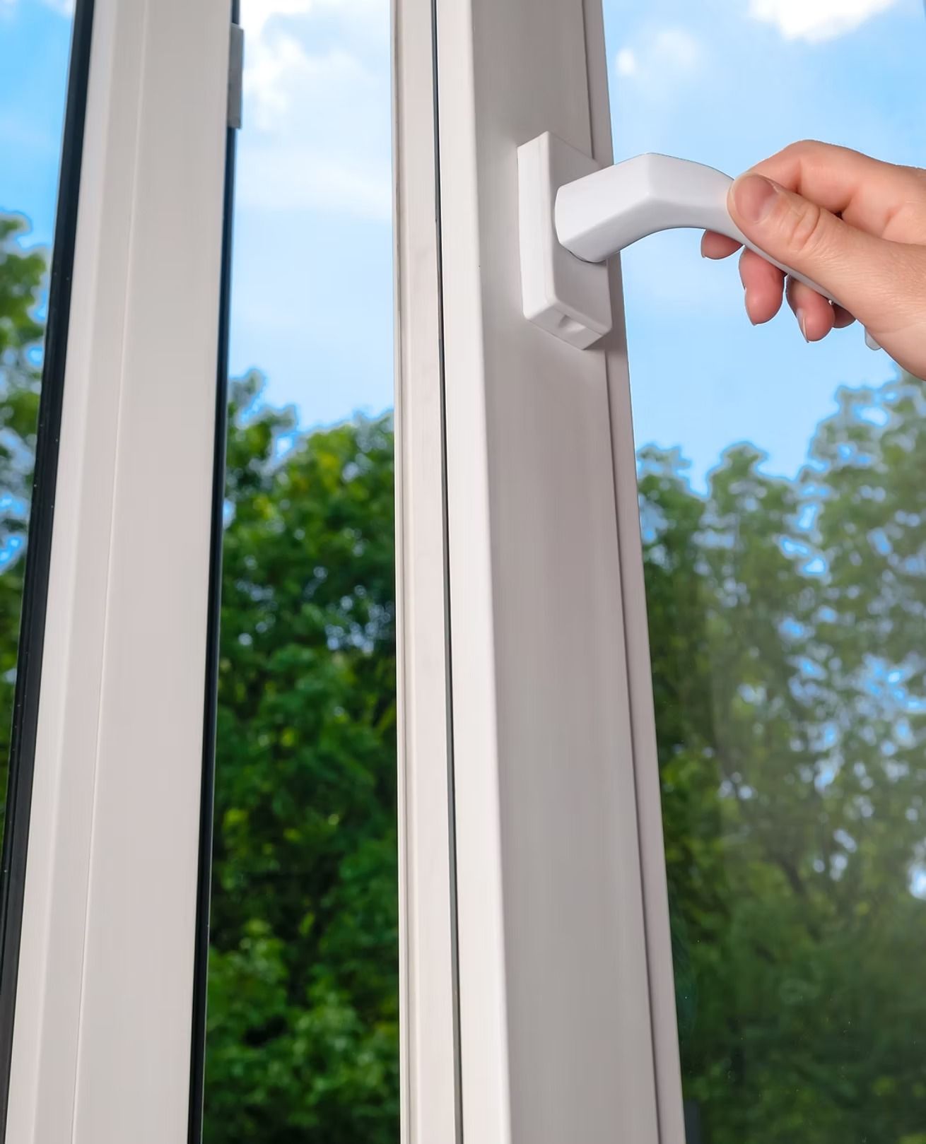 Hand opening a white window latch on a glass door with trees outside