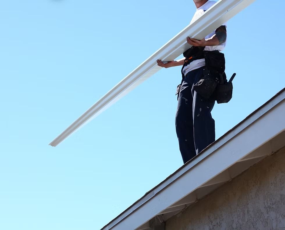 Worker on a roof carrying a long white beam against a blue sky