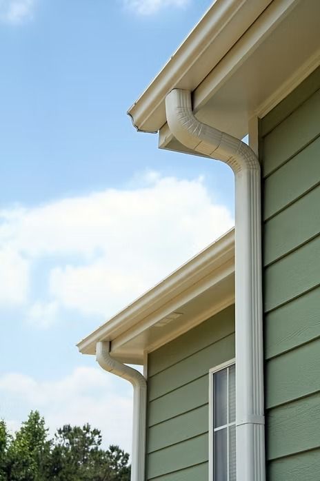 Green house exterior with white gutters under a blue sky