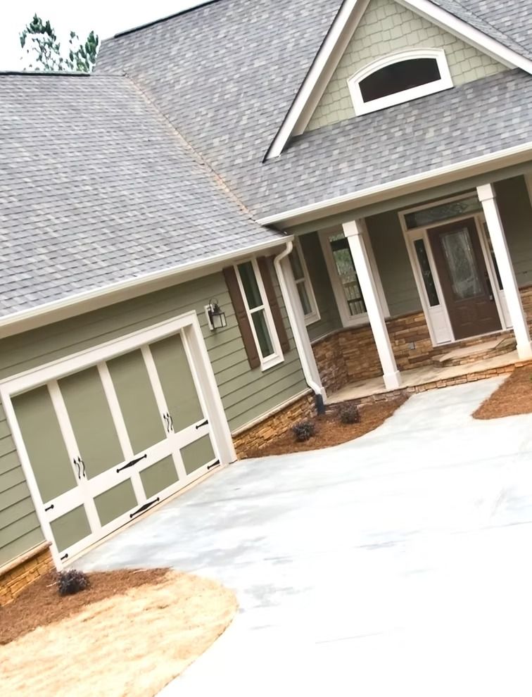Suburban house with beige garage, green siding, covered porch, and a white driveway under construction