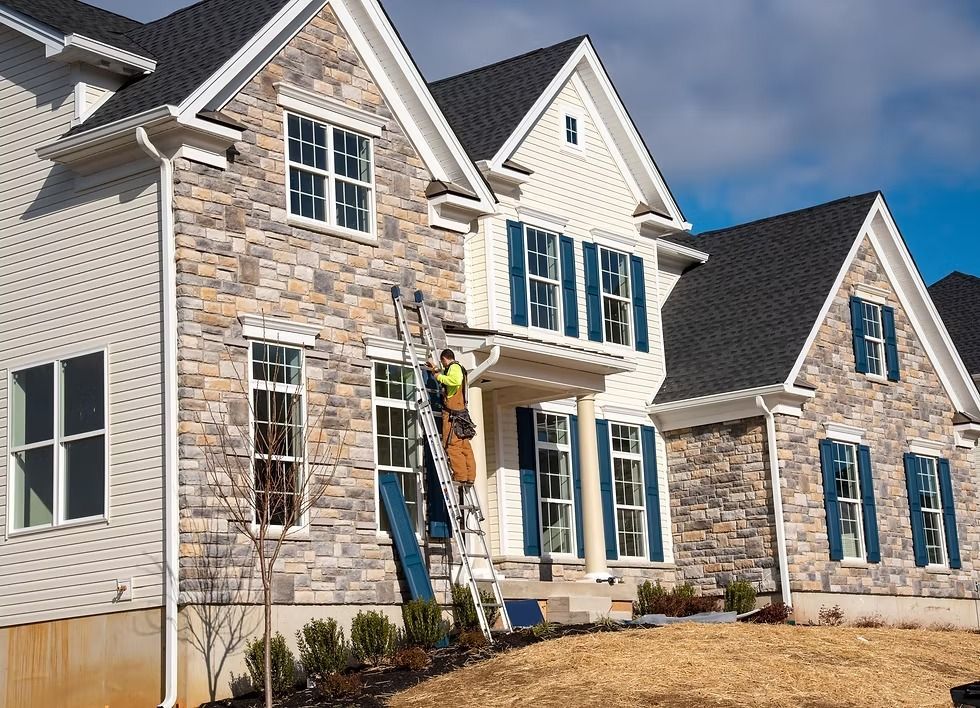New two-story house with stone and white siding, blue shutters, and a ladder by the front entrance