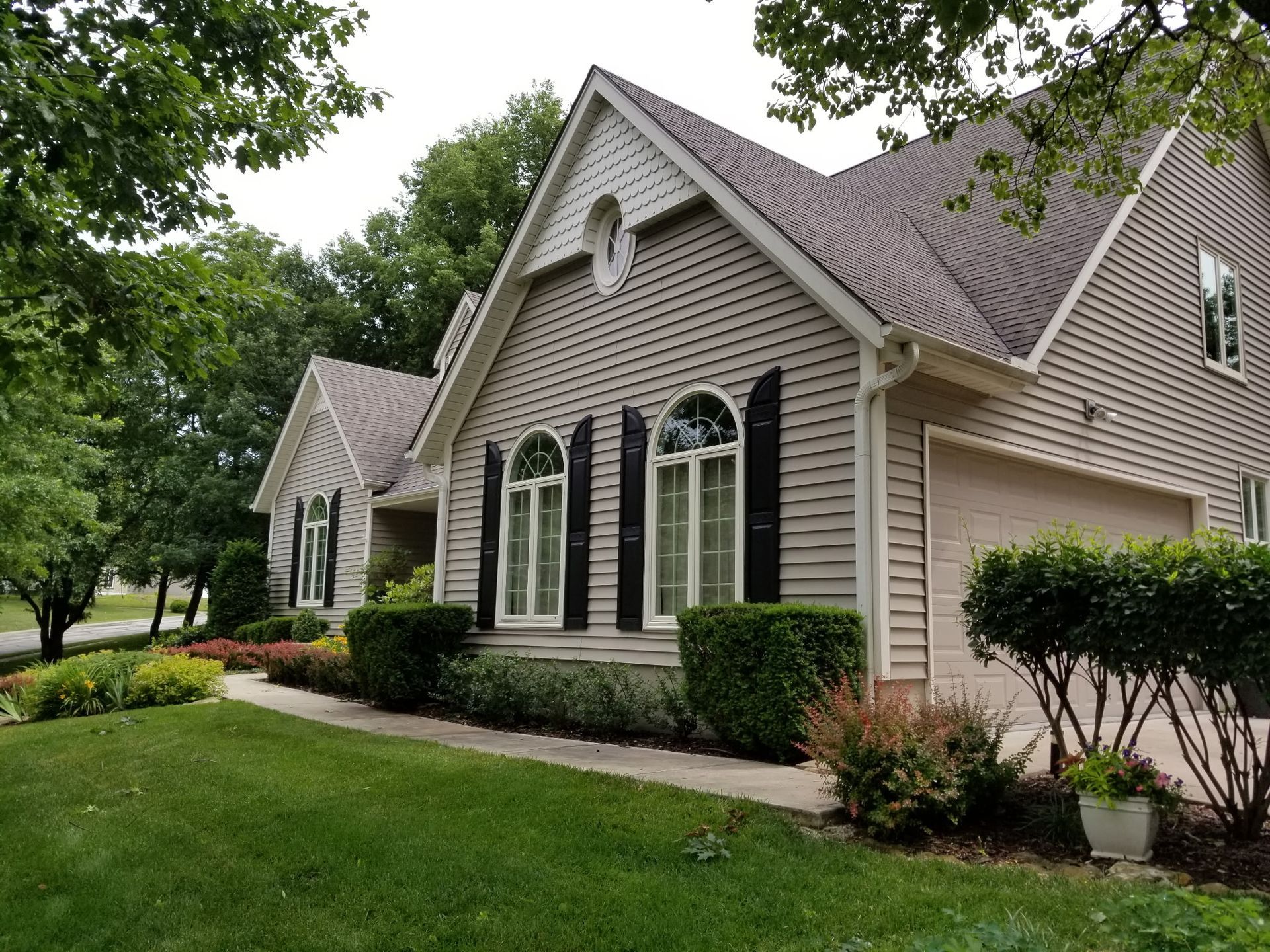 Suburban brick house with gabled roof, arched windows, green lawn, and shrubs
