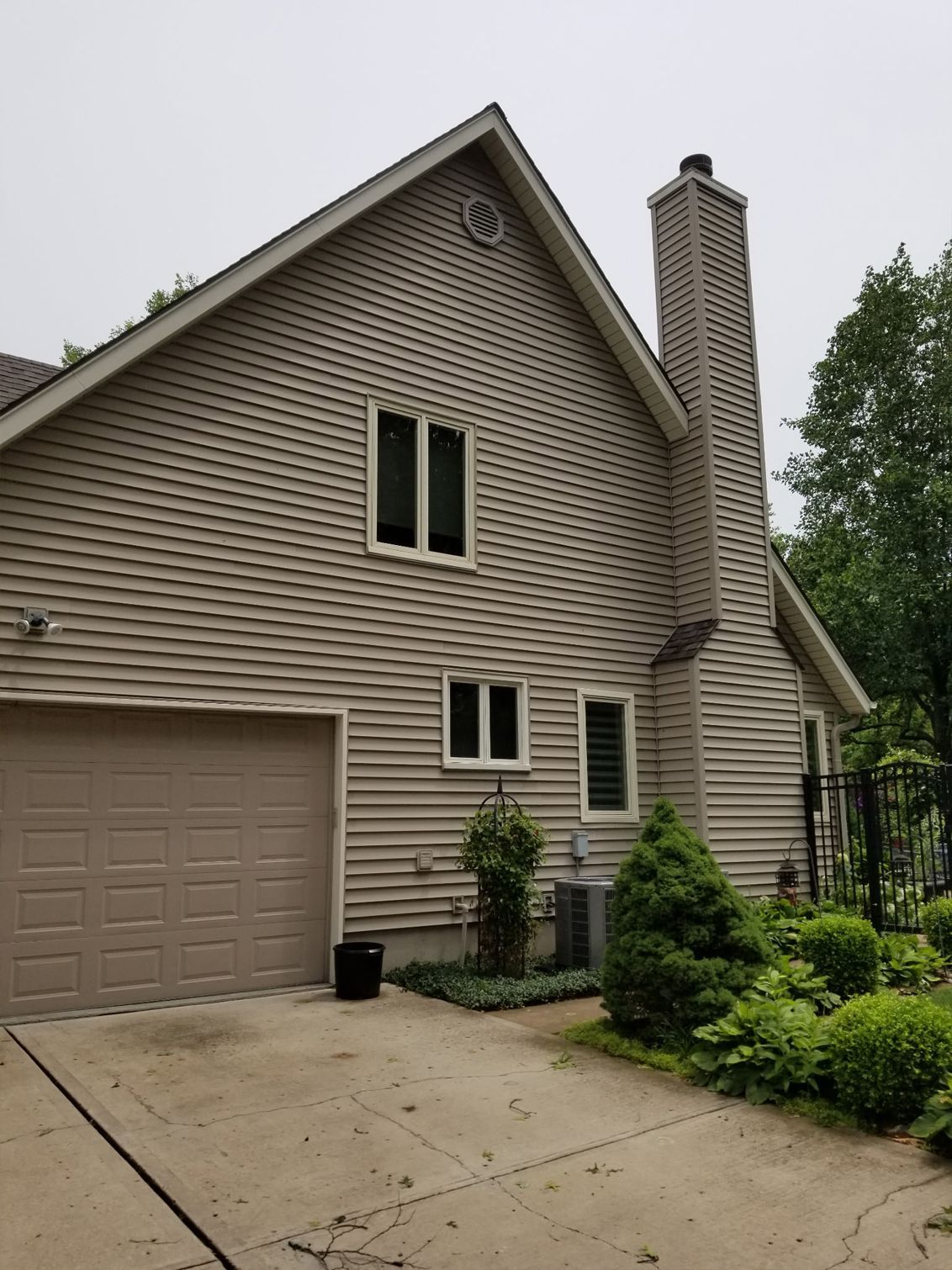 Suburban house exterior with beige siding, garage, driveway, and landscaped front yard under cloudy sky