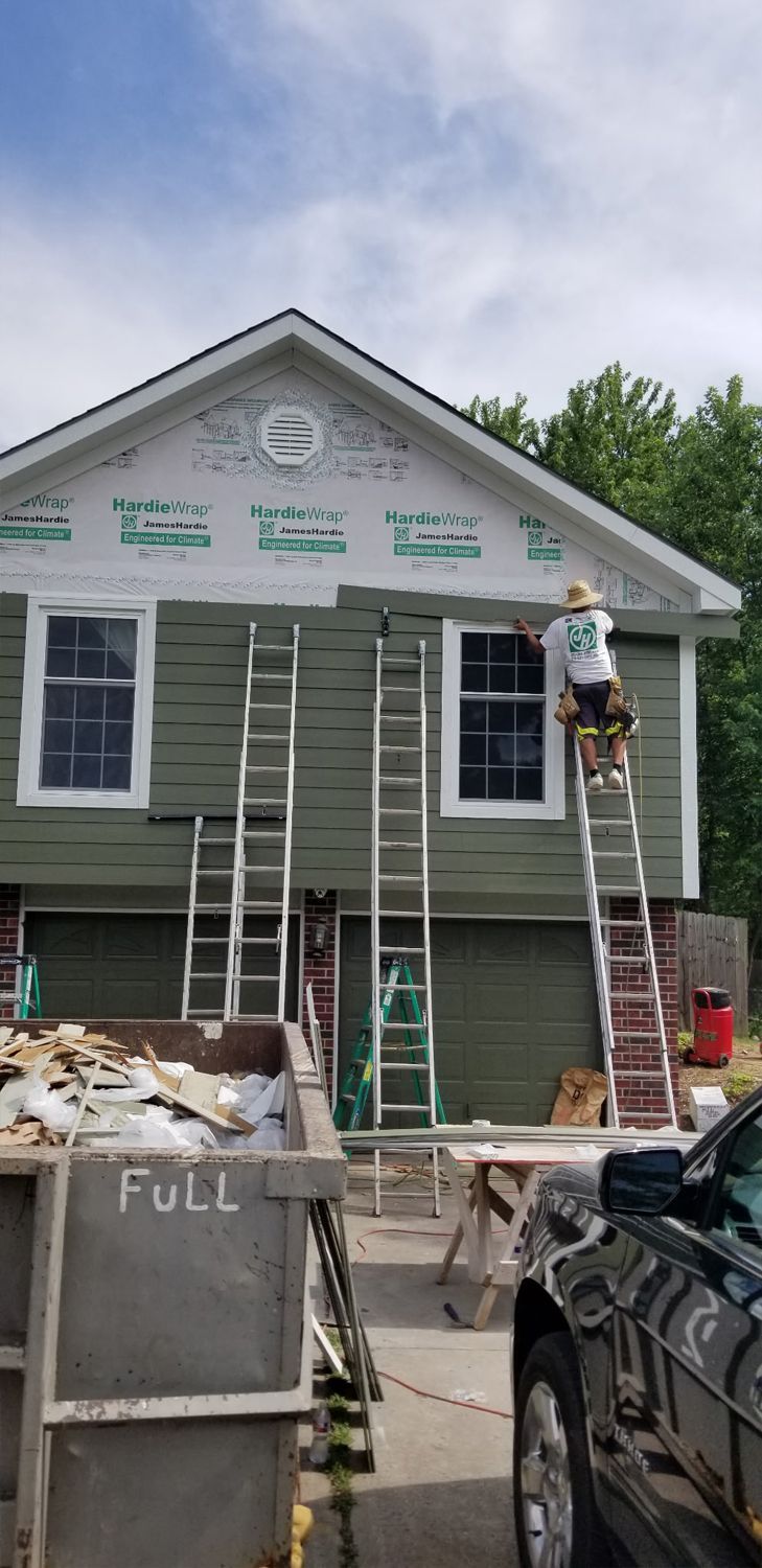 Workers on ladders painting a small green house under construction.