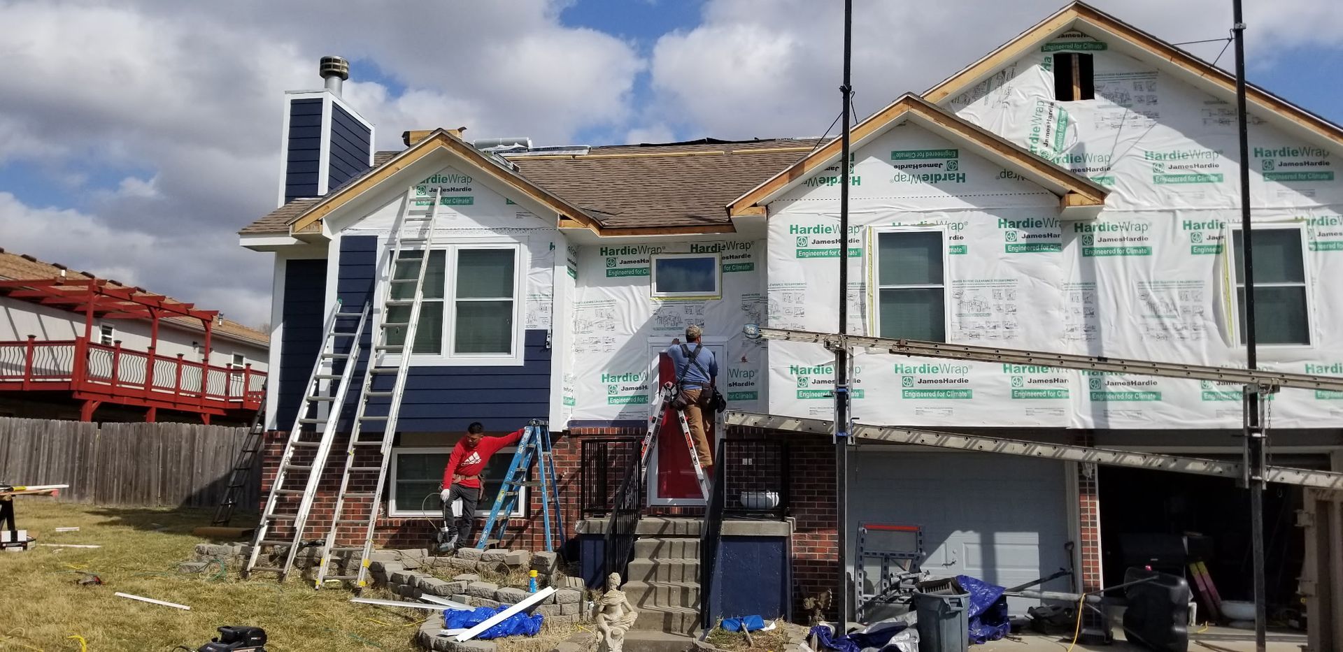 House under renovation with workers on ladders and scaffolding beside a bridge