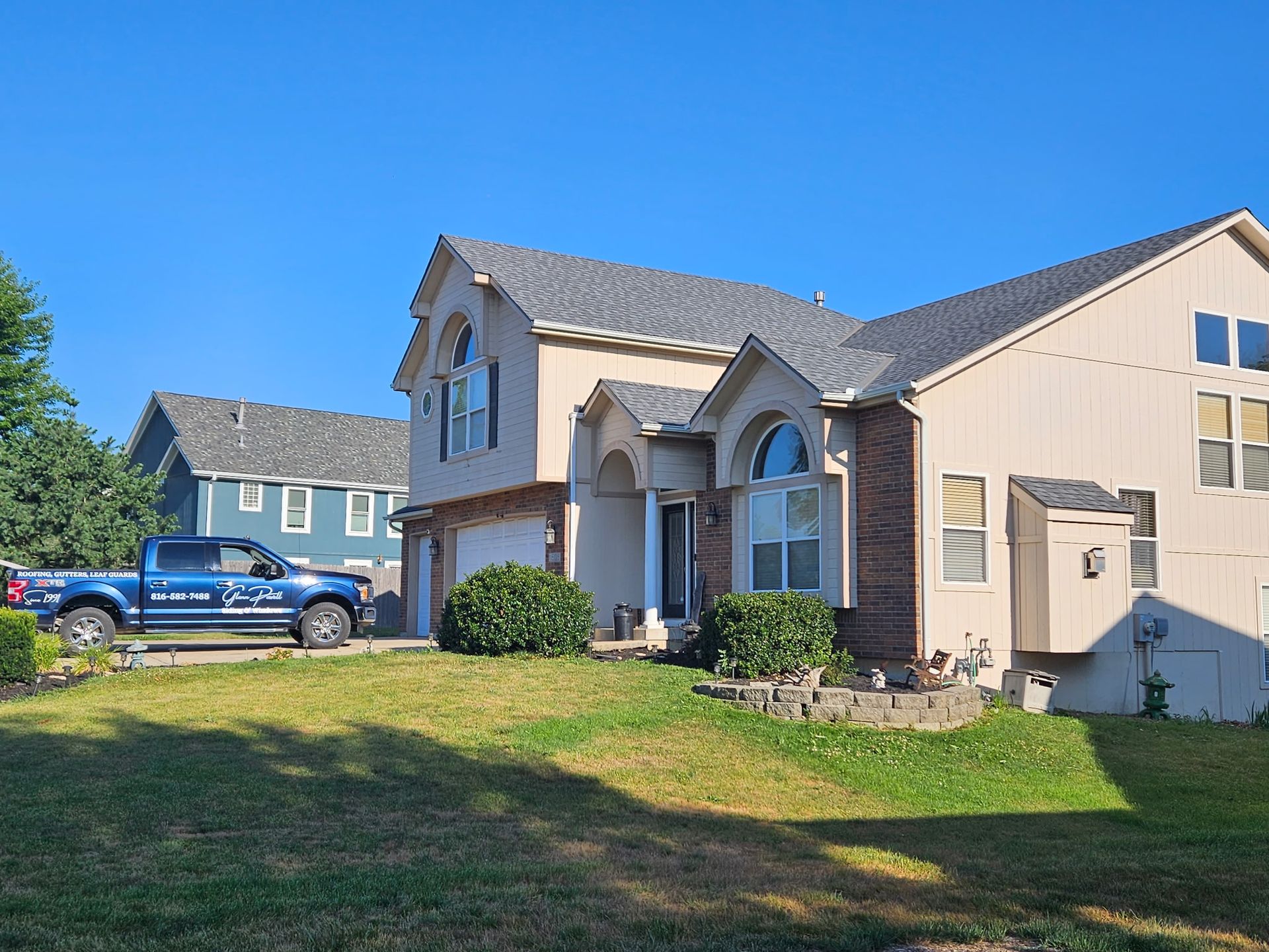 Suburban house with beige siding, blue car parked in front, and a grassy lawn on a sunny day