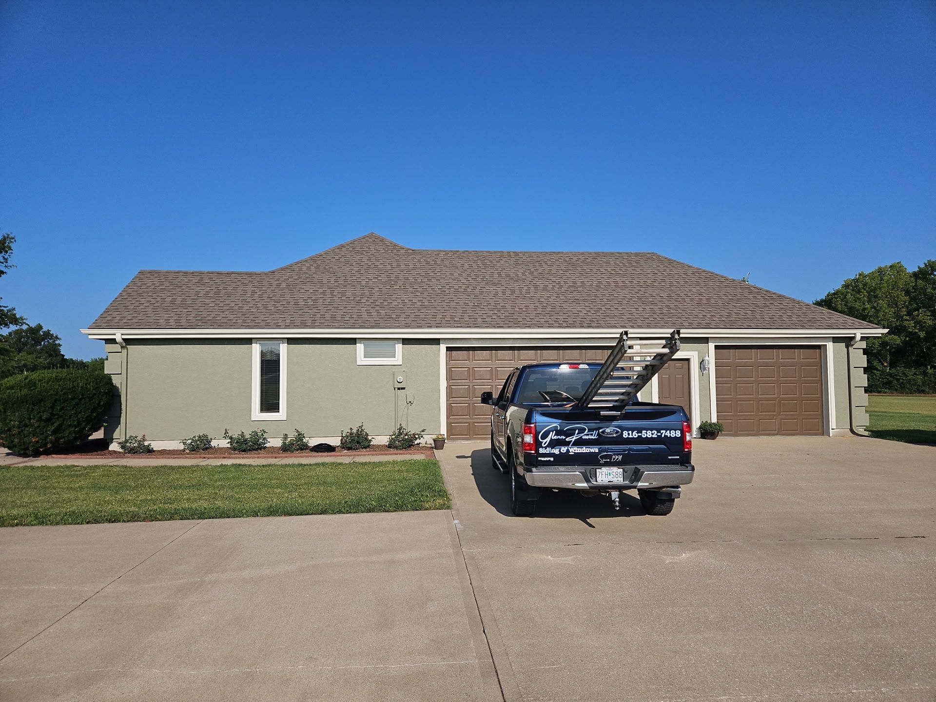 Blue pickup truck parked in a suburban driveway in front of a beige house with a tiled roof.