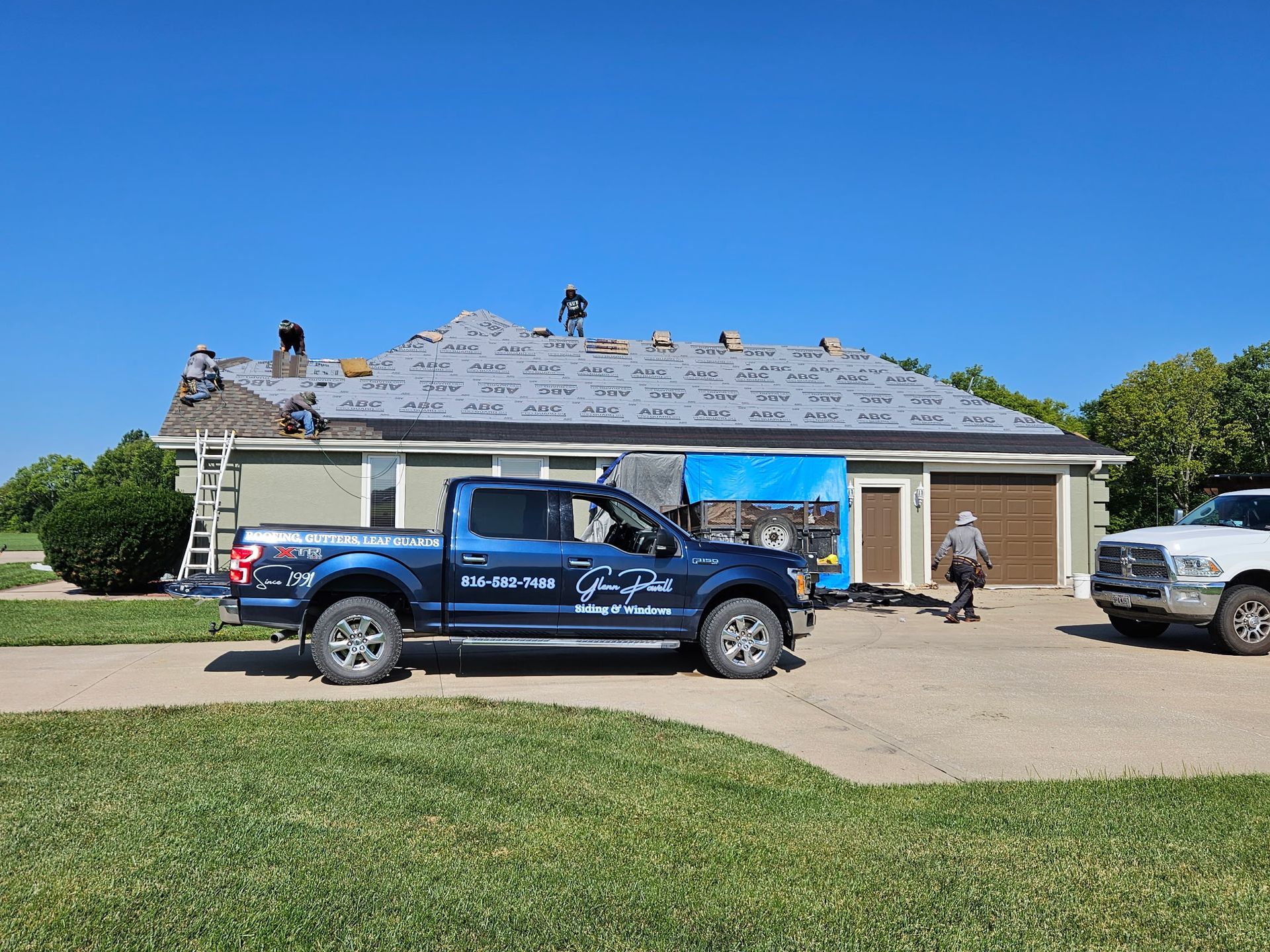 Two workers on a blue truck beside a house with a damaged roof under repair