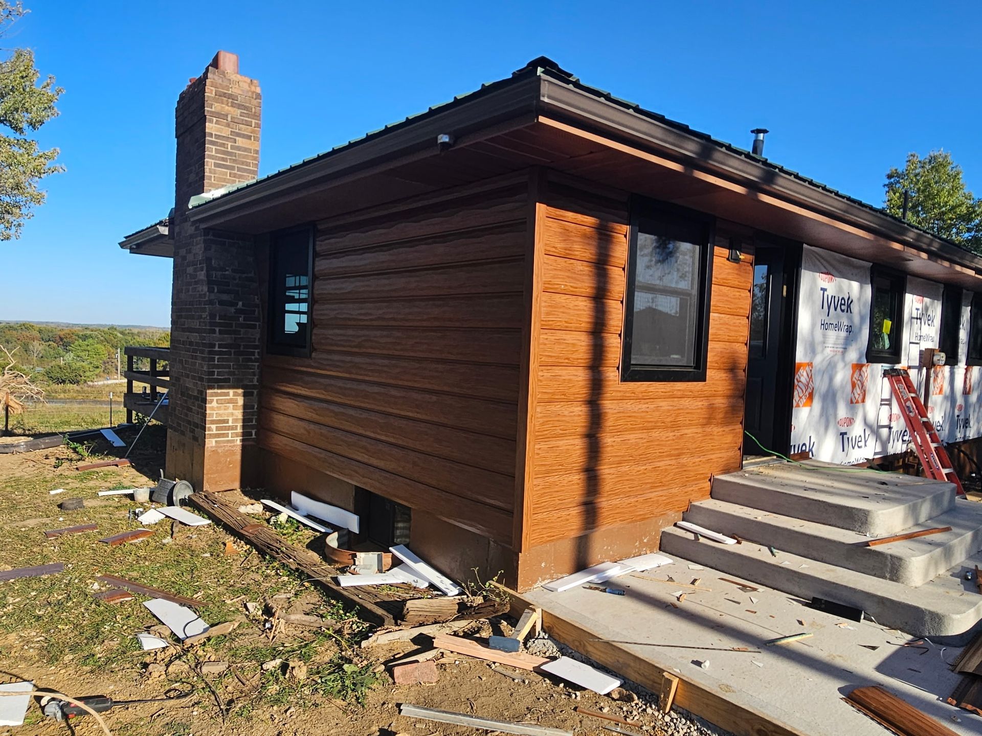 Brown house exterior with damaged steps, stone chimney, and construction debris in the yard