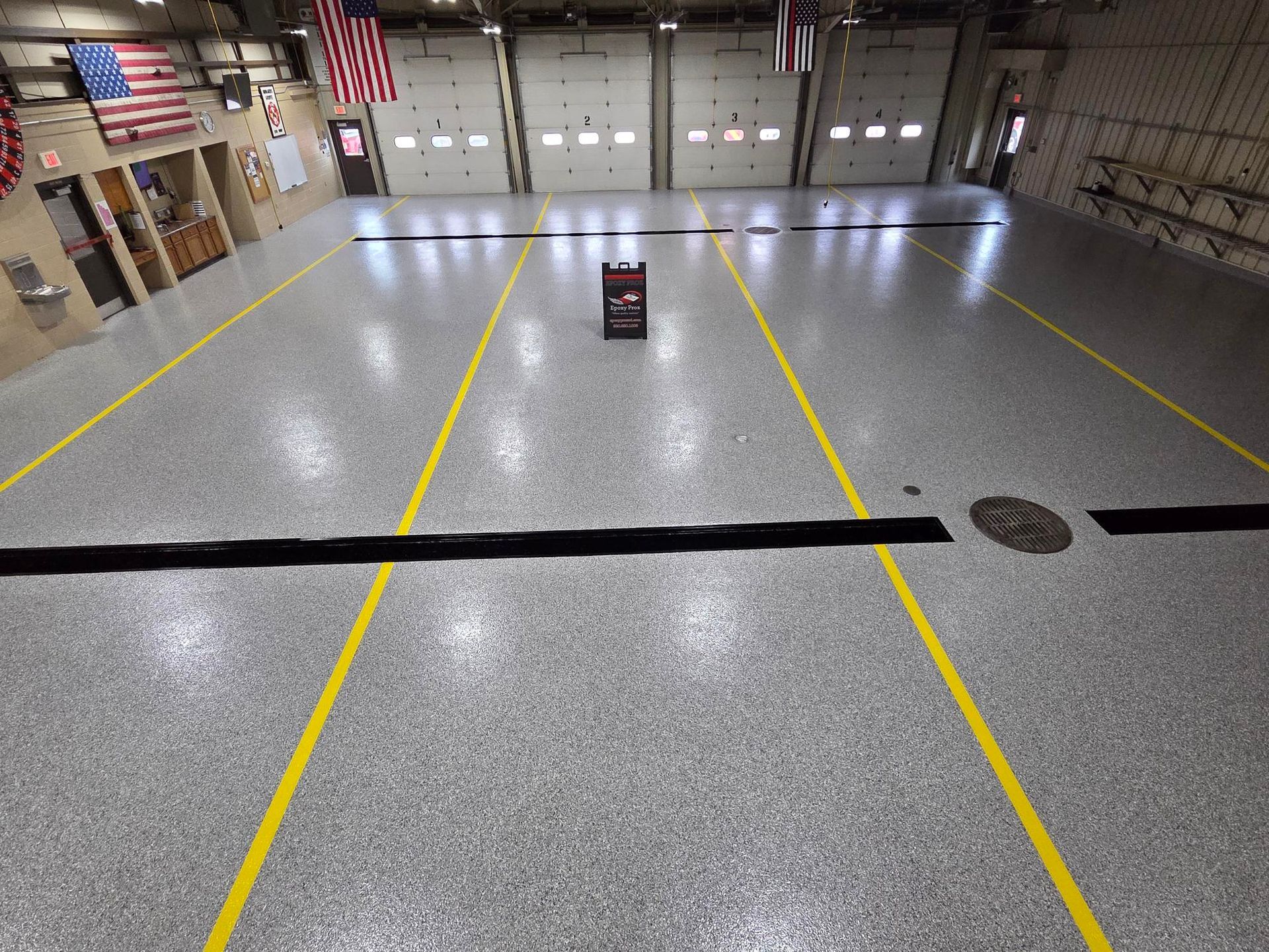 Empty gymnasium floor with yellow court lines and a small sign near center, American flags on the wall
